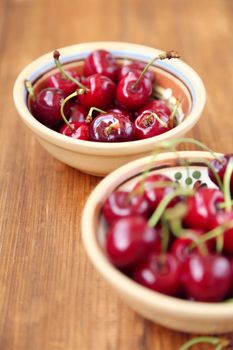 many ripe raw wet sweet cherry in dish on wooden background