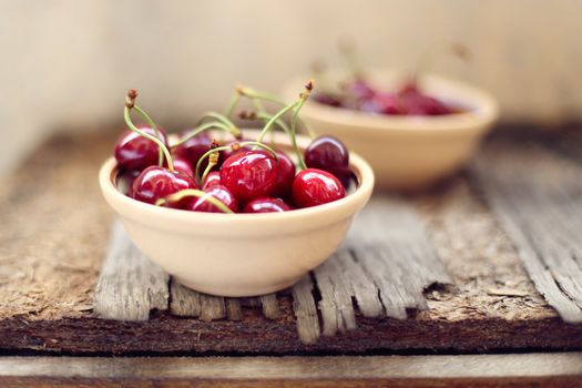 many ripe raw wet sweet cherry in dish on wooden background