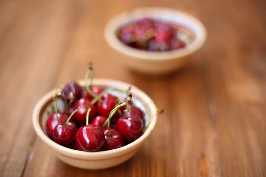 many ripe raw wet sweet cherry in dish on wooden background