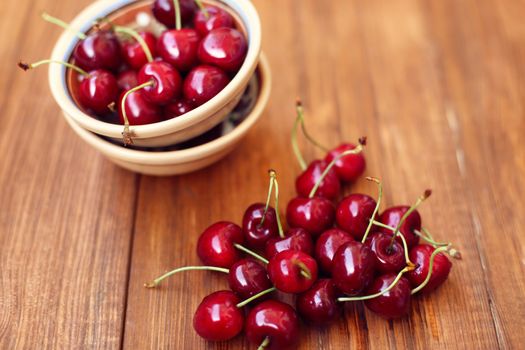 many ripe raw wet sweet cherry in dish on wooden background