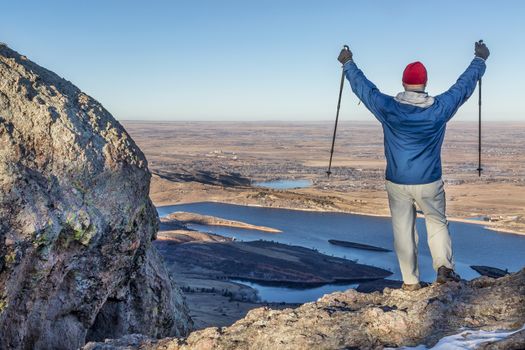 a male hiker with trekking poles overlooking Horsetooth Reservoir from Arthur's Rock near Fort Collins, Colorado, a typical winter scenery without snow