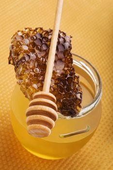 Honey in glass jar with wooden honey spoon and honey comb on golden honey comb background. Healthy honey eating.