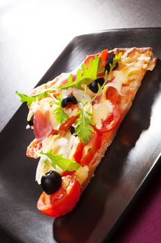 Delicious hot pizza piece triangle on black plate on table, minimal contemporary style. 