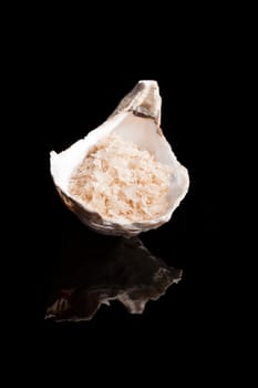Smoked himalaya salt crystals in beautiful seashell isolated on black background. 