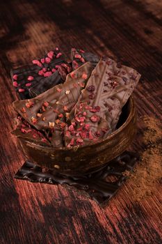 Luxurious dark and milk chocolate pieces in wooden bowl on wooden background. Sweet chocolate dessert eating. 