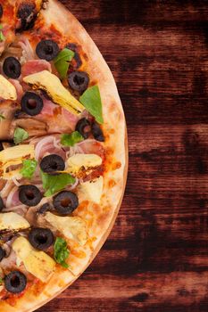 Delicious colorful pizza with tomatoes, melted cheese, black olives, onions, ham and fresh herbs on dark brown wooden background. Culinary mediterranean pizza eating.