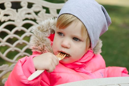 Child eating waffles with chocolate in a spring park