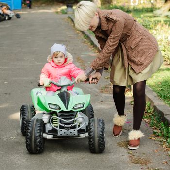 Little girl riding toy car in autumn park