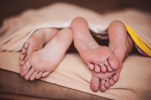 couple barefoot in bed under blanket no face 