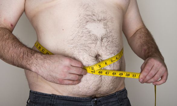 Young man putting a measuring tap against his abdoment trying to see how large he is
