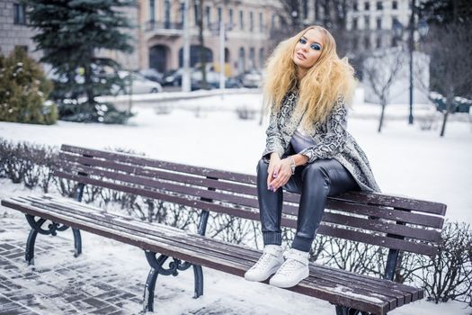 Blonde young girl is sitting on a bench