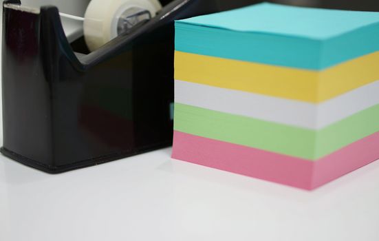 Office supplies was placed on table at office, such as adhesive tape and note pads.                               