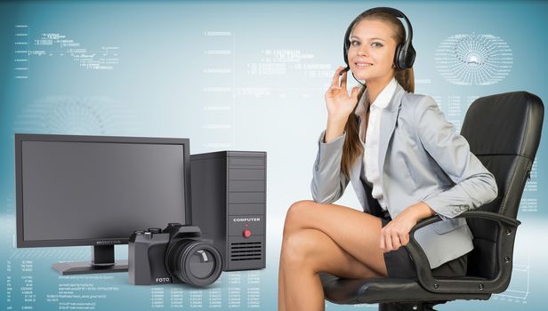 Businesswoman in headset sitting on office chair, her hand on microphone, looking at camera, smiling. Desktop computer and camera beside. Hi-tech graphs with various data as backdrop