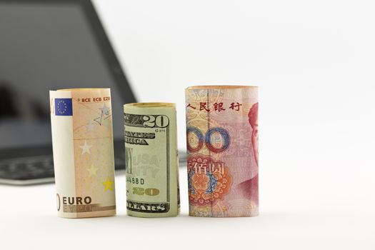 Three currencies, euro, United States dollar, and Chinese yuan, placed before tablet and keyboard. 