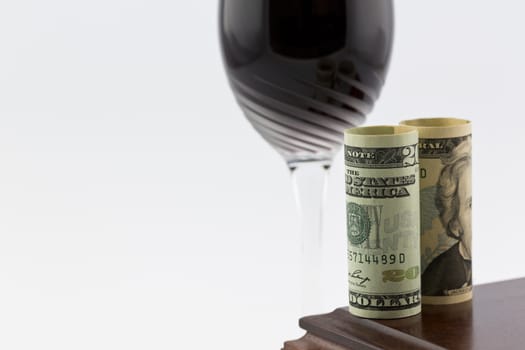 American currency placed on polished wood box in front of stem glass with red wine; horizontal image with white copy space; 