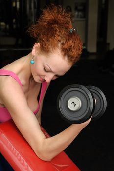 Girl doing biceps exercise with dumbbell in the gym