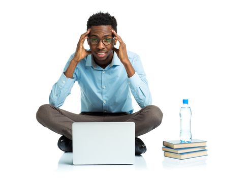 African american college student with headache sitting on white background with laptop and some books