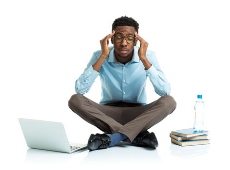 Happy african american college student in stress sitting with laptop, books and bottle of water on white background