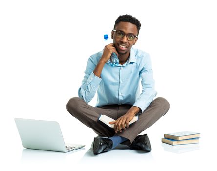 Happy african american college student sitting with laptop, books and bottle of water on white background