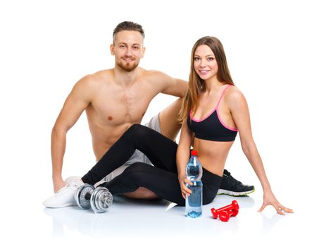 Athletic couple - man and woman after fitness exercise sitting with dumbbells on the white background