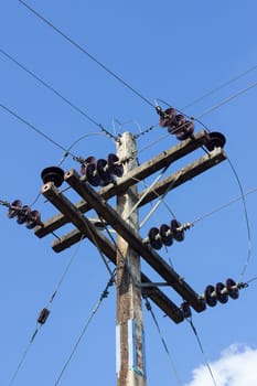 electrical post by the road with power line cables, against blue sky with cloud