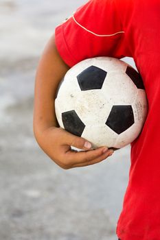 boy with red t-shirt holding dirty black white football or soccer sport ball in hand