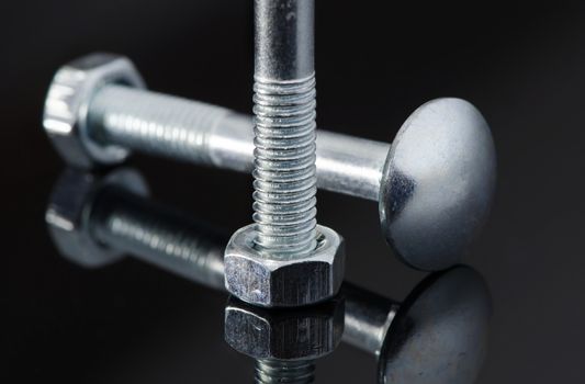 Two metal screws with nice reflection on black background.