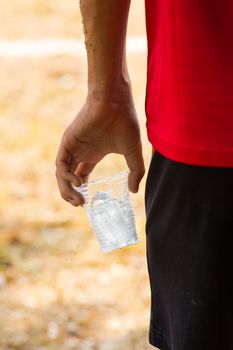hand of athlete holding glass of iced water against strong sunlight background, silhouette
