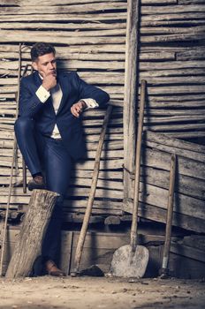 Fashion image in rustic area with young man checking the time against wooden fence