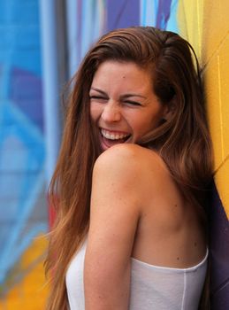 Young woman standing in front of a colorful background and laughing.