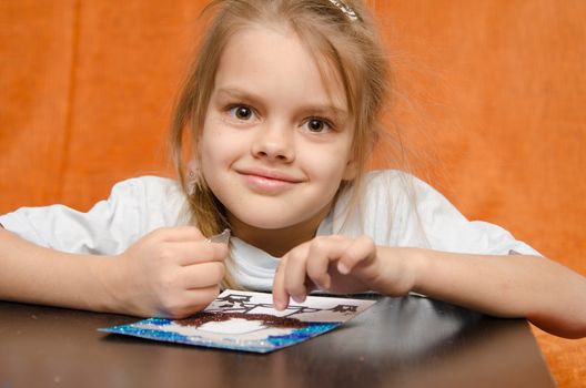 five year old girl sitting at the table and collects sand applique
