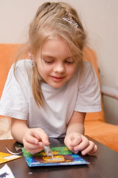 five year old girl sitting at the table and collects sand applique