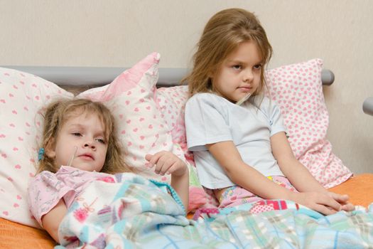 Two girls and four to six years lying in bed meryat temperature thermometer