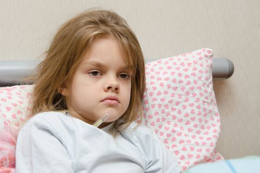 Six-year diseased girl sitting in bed and will measure the temperature of the thermometer