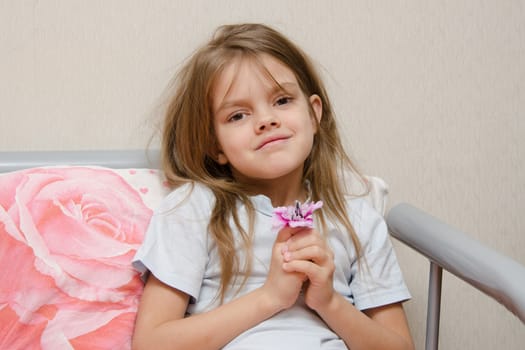 Touching five year old girl sitting in bed with a flower in hands