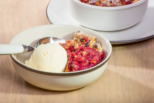 Freshly baked mixed berry crumble in a small dish, served with vanilla ice cream.