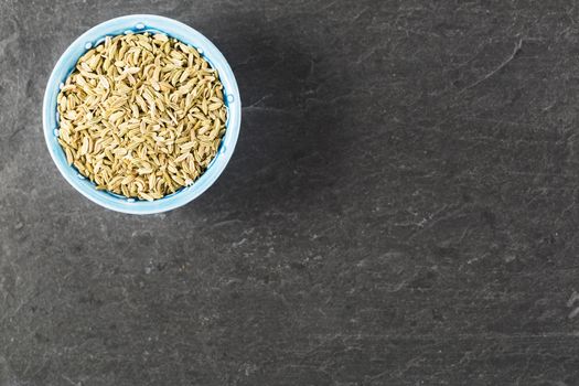 Bowl of fennel seeds on stone surface with copy space.