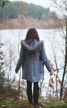 Young girl with her hair stands near the water in the cold season. Back view