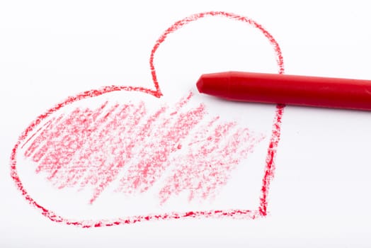 Closeup of a red pencil drawing a heart. On white paper.