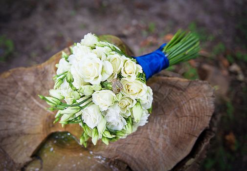 Wedding golden rings on bridal bouquet with gentle white roses on the stump