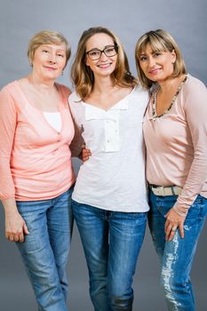 Three generations of attractive women with blond hair and a striking family resemblance posing together arm in arm looking at the camera with friendly smiles