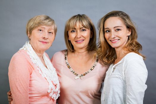 Three generations of attractive women with blond hair and a striking family resemblance posing together arm in arm looking at the camera with friendly smiles