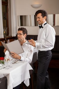 Waiter serving a young couple seated at a table holding menus in a restaurant waiting as they make their choice and place their order