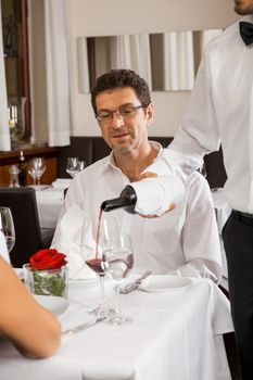 Waiter serving a young couple seated at a table holding menus in a restaurant waiting as they make their choice and place their order