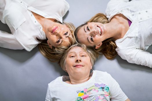 Three generations of attractive women with blond hair and a striking family resemblance posing together arm in arm looking at the camera with friendly smiles