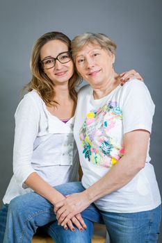 Loving grandmother and teenage granddaughter posing for a portrait holding hands and smiling at the camera, on a grey studio background