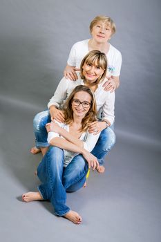 Three generations of attractive women with blond hair and a striking family resemblance posing together arm in arm looking at the camera with friendly smiles