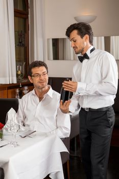 Waiter serving a young couple seated at a table holding menus in a restaurant waiting as they make their choice and place their order