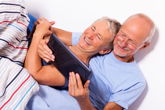 Senior Couple Relaxing in Bed with Tablet Computer and Newspaper