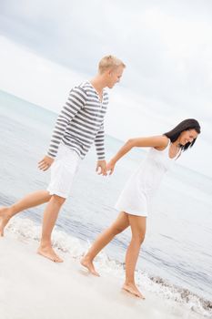 Caucasian happy young couple holding hands while walking barefoot on the beach in a romantic travel destination